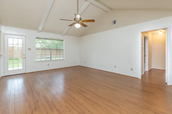 an empty room with wooden floor fan and windows