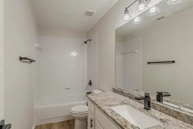 a bathroom with a granite countertop sink a toilet a mirror a bathtub and shower