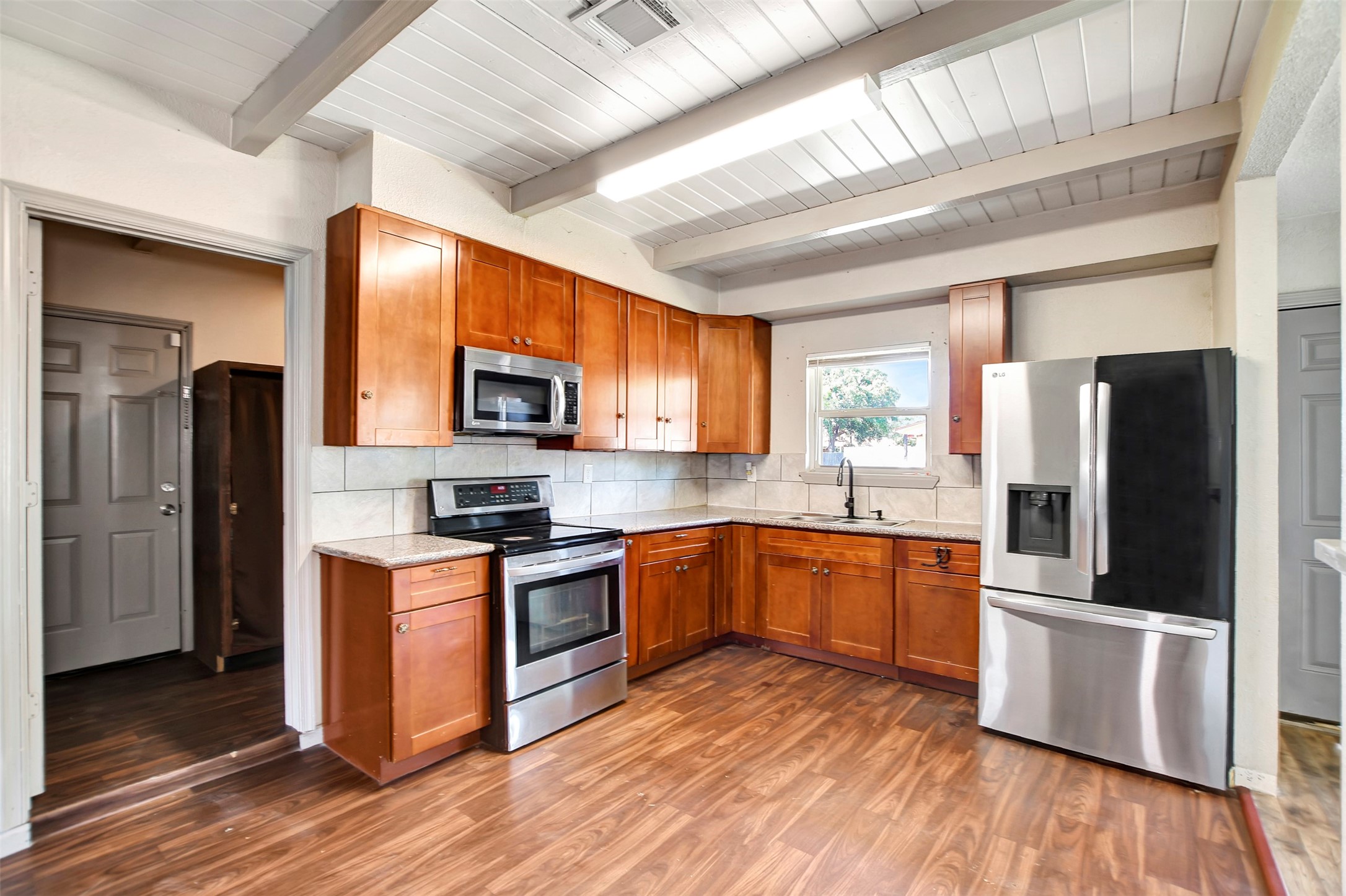 a large kitchen with stainless steel appliances granite countertop a stove a sink dishwasher a refrigerator and a microwave oven with wooden floor