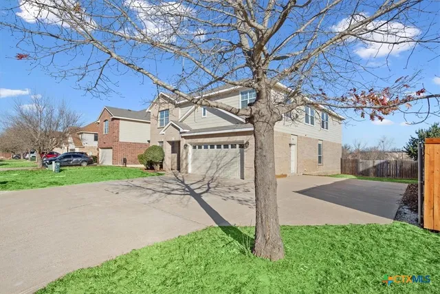 a view of a brick house with a small yard and large tree