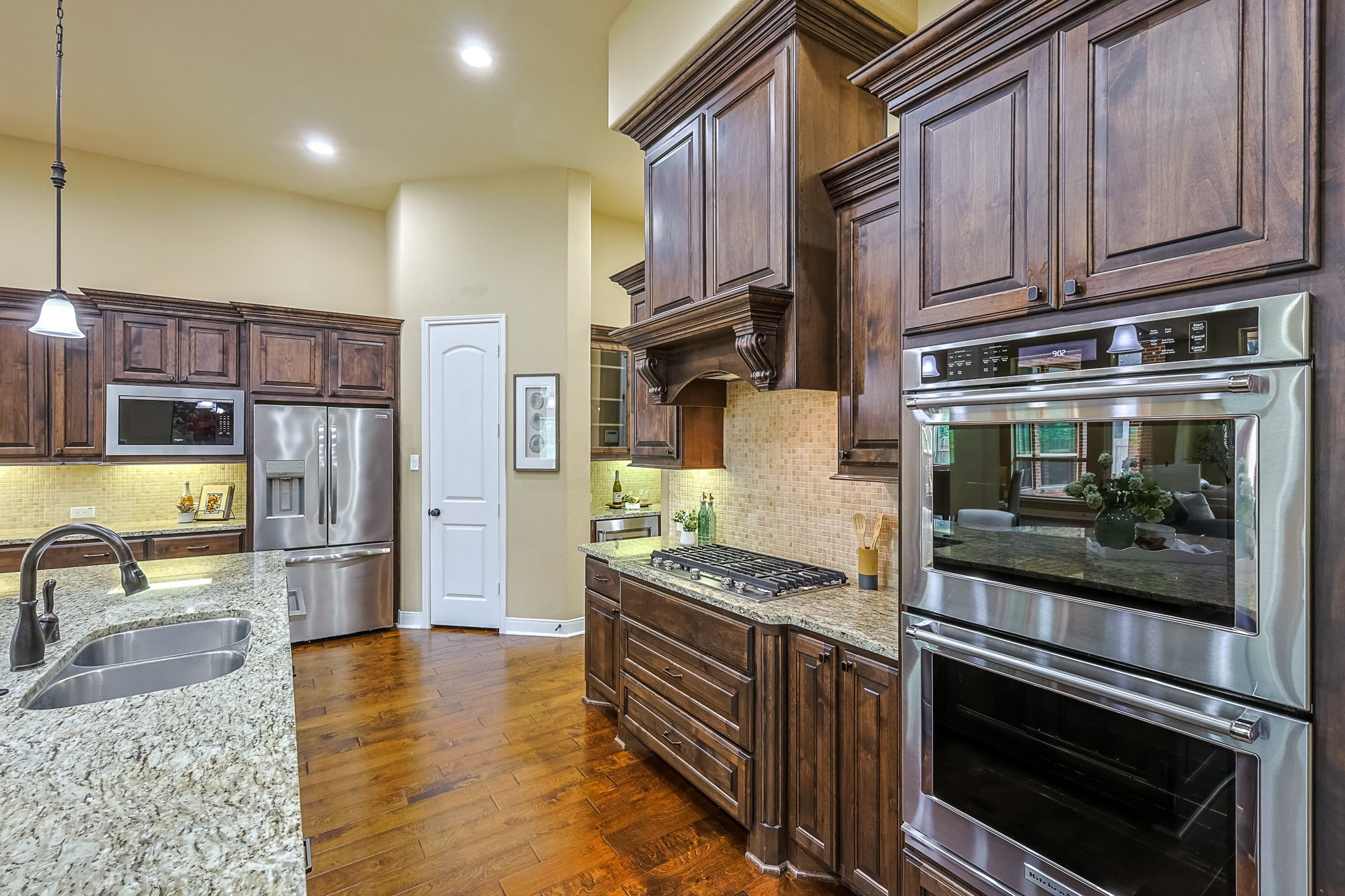 515 Mill Creek Road Pinehurst, TX 77362 - Photo 18 of 48 Spacious kitchen featuring rich wooden cabinetry, stainless steel appliances, and granite countertops. The layout includes a double oven, gas cooktop, and a large island with a sink, perfect for cooking and entertaining. The warm lighting and hardwood floors add a cozy touch.