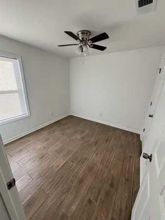 an empty room with wooden floor fan and windows