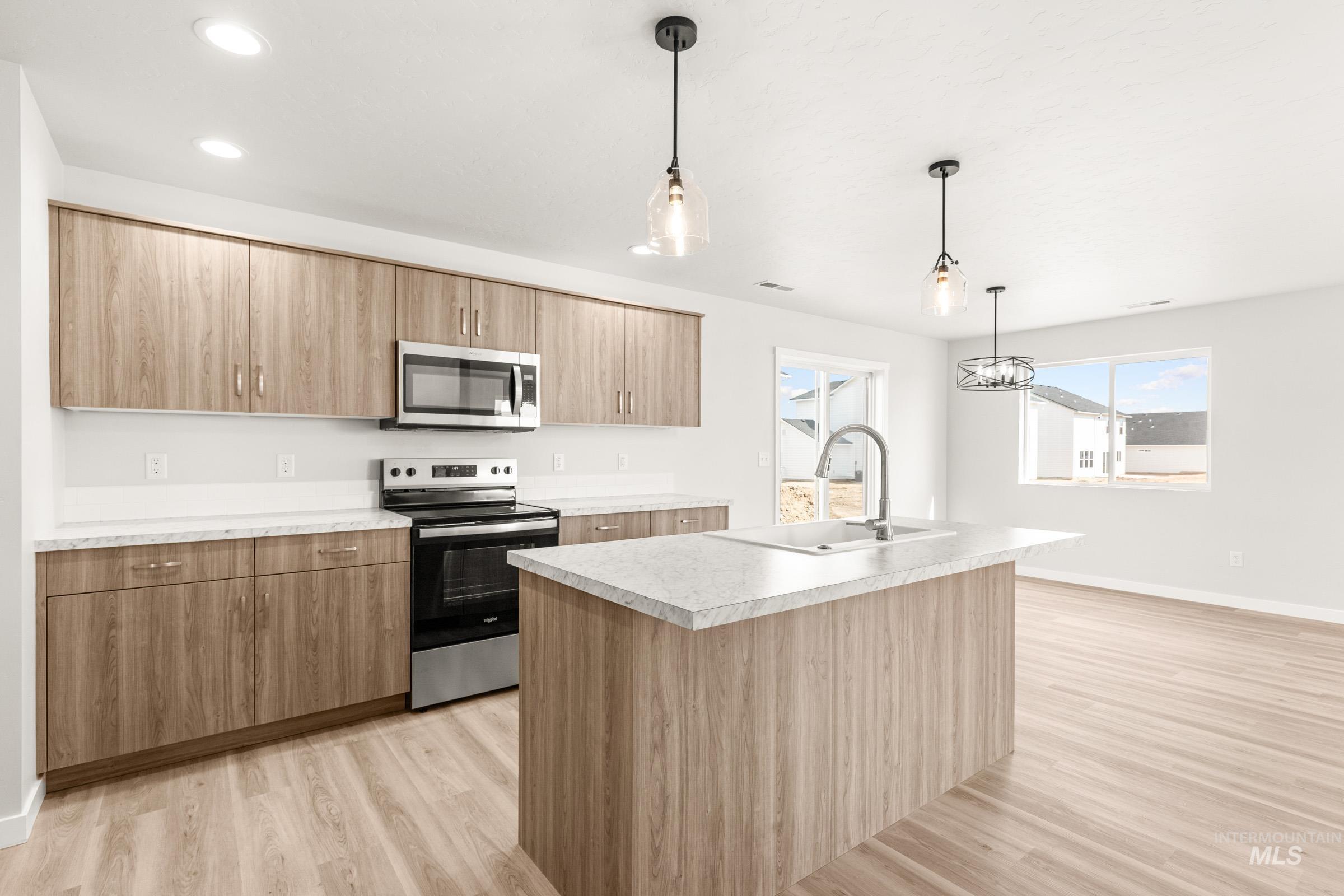 13716 Redway Court Caldwell, ID 83607 - Photo 3 of 18 Kitchen with stainless steel appliances, an island with sink, hanging light fixtures, light wood-type flooring, and light countertops