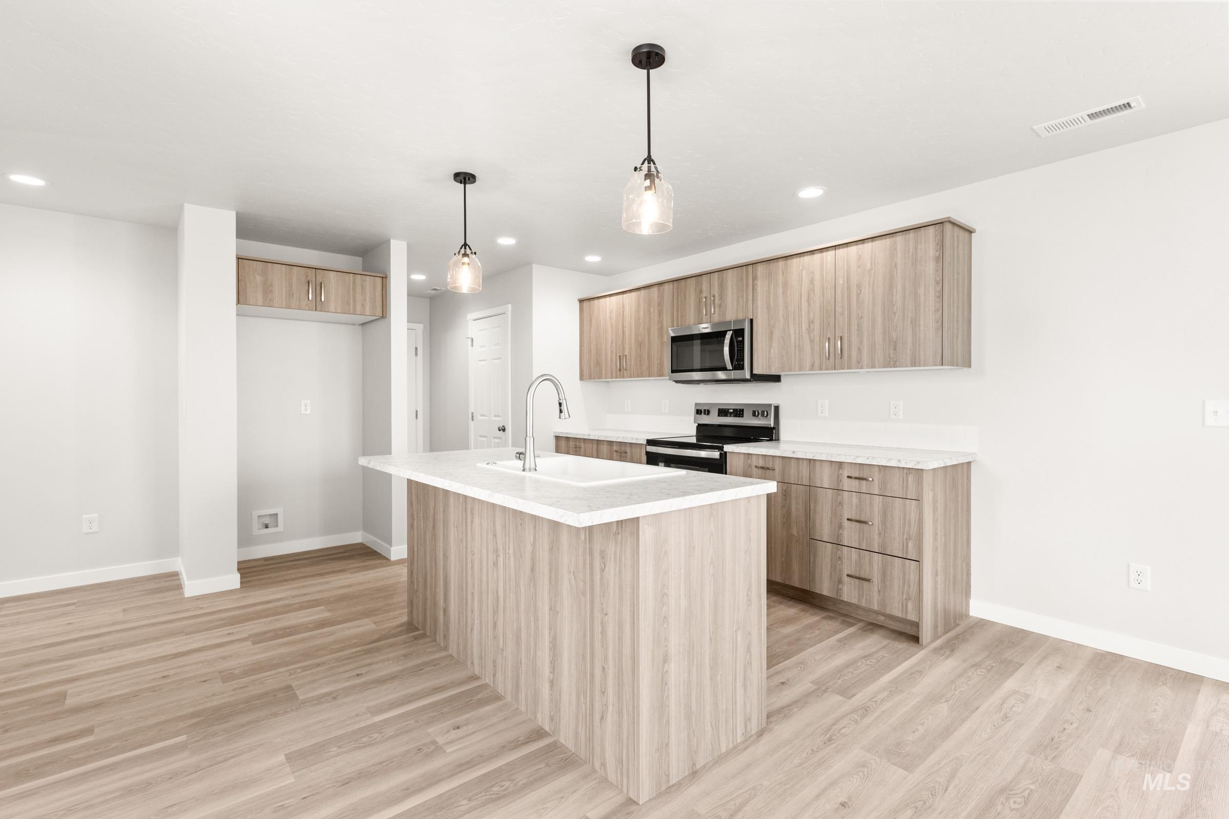 13716 Redway Court Caldwell, ID 83607 - Photo 4 of 18 Kitchen with light wood-style flooring, stainless steel appliances, an island with sink, and hanging light fixtures