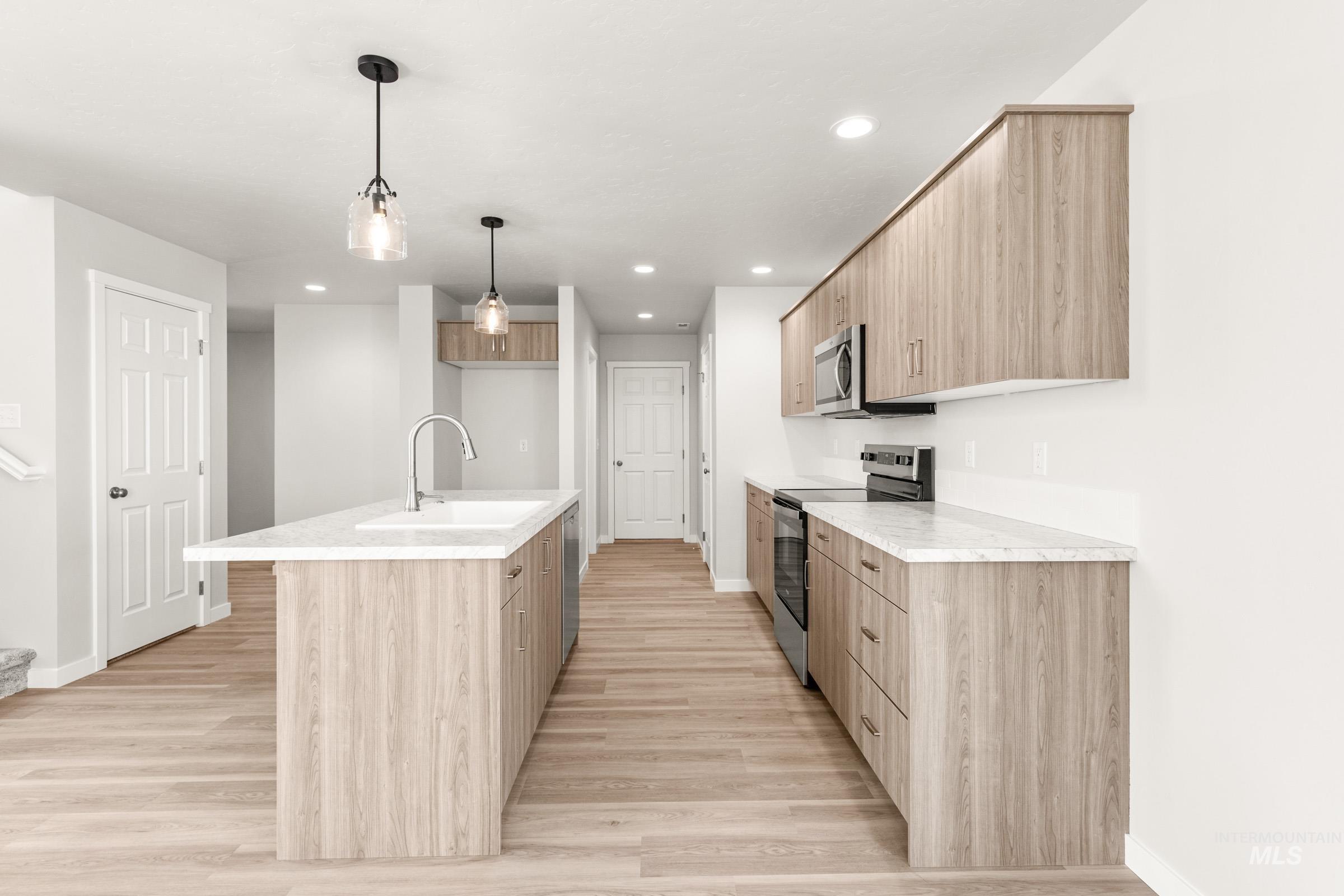 13716 Redway Court Caldwell, ID 83607 - Photo 5 of 18 Kitchen with a center island with sink, stainless steel appliances, light wood-type flooring, light wood finish cabinetry, and hanging light fixtures