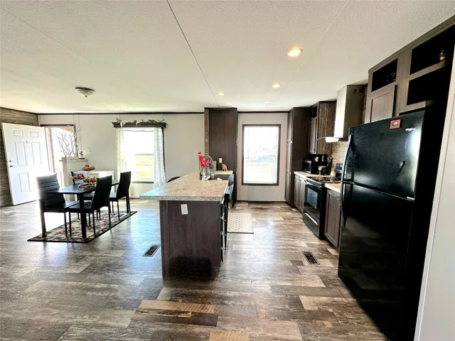 a kitchen with stainless steel appliances kitchen island granite countertop a refrigerator a stove a sink a dining table and chairs with wooden floor