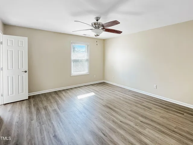 an empty room with wooden floor chandelier fan and windows