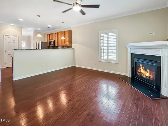 a view of an empty room and kitchen with wooden floor