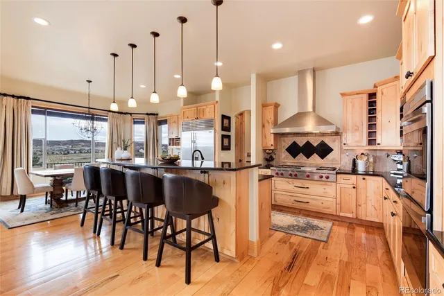 a kitchen with stainless steel appliances kitchen island granite countertop a stove a refrigerator a oven a sink with a dining table and chairs with wooden floor