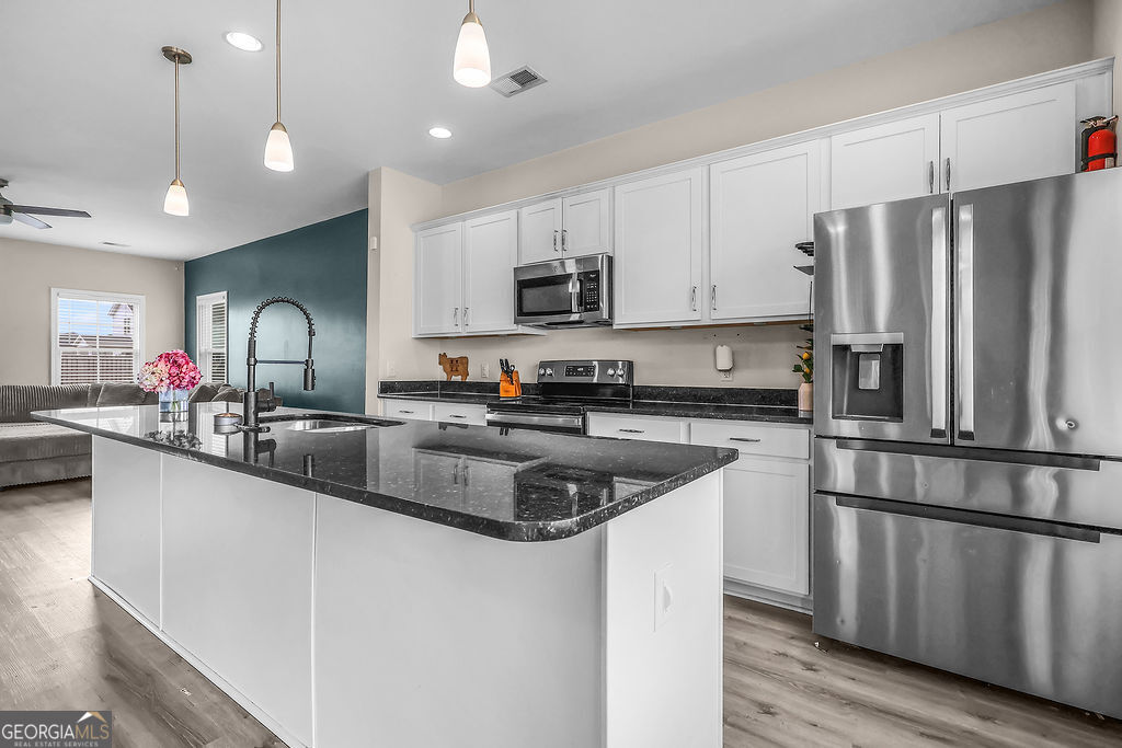 231 Caroline Way Guyton, GA 31312 - Photo 14 of 47 a kitchen with stainless steel appliances granite countertop a sink a stove a refrigerator cabinets and a wooden floor
