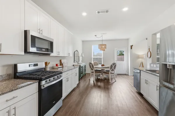 a kitchen with granite countertop a stove top oven a sink dishwasher a dining table and chairs with wooden floor