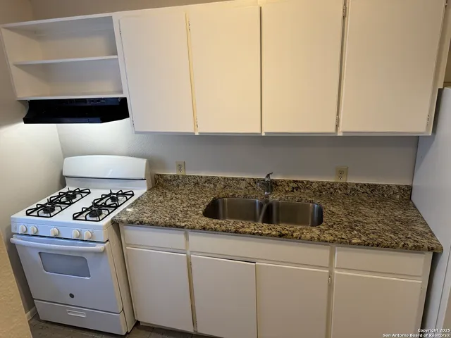 a kitchen with granite countertop a sink a stove and cabinets
