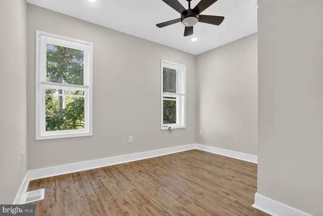 an empty room with wooden floor fan and windows