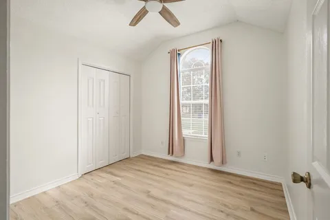 an empty room with wooden floor fan and windows