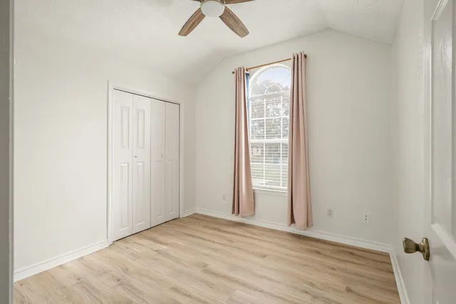an empty room with wooden floor fan and windows