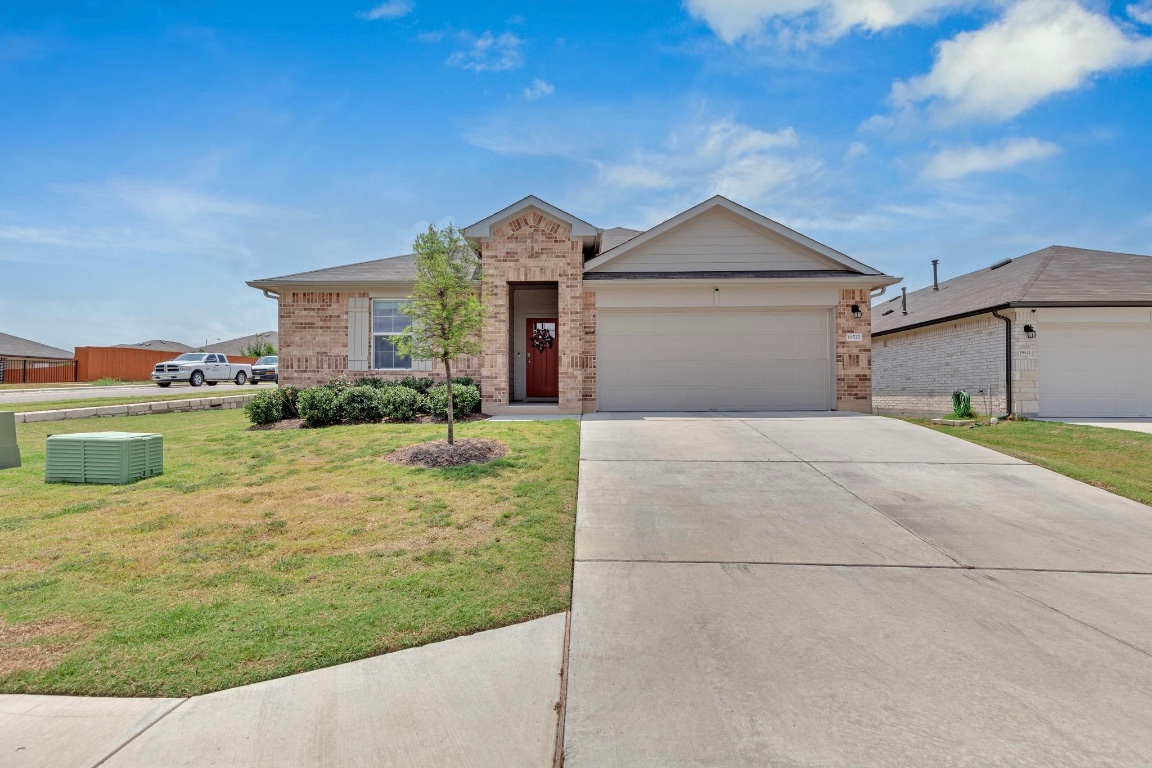 Ranch-style home featuring an attached garage, concrete driveway, brick siding, and a front yard