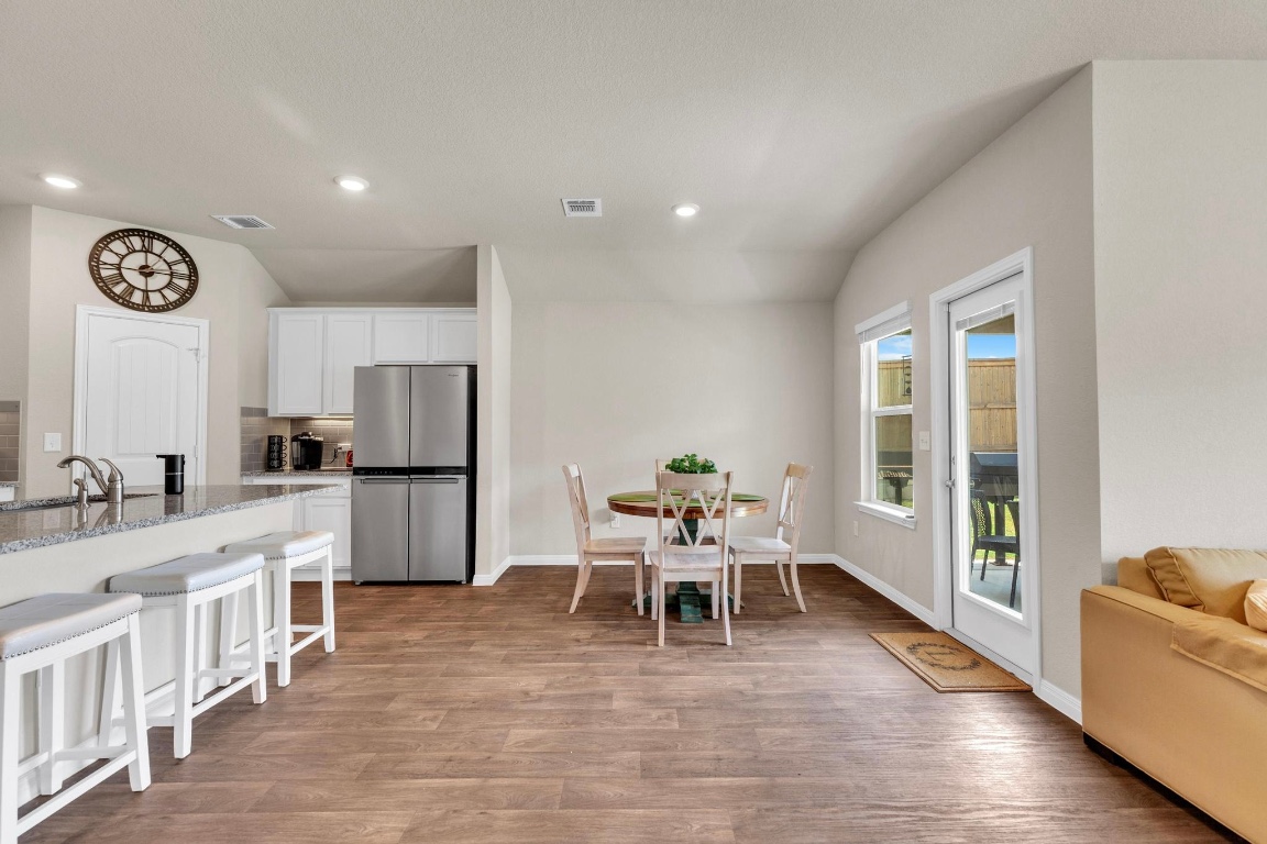 19525 Abigail Fillmore Road Manor, TX 78653 - Photo 11 of 40 Kitchen with light stone countertops, white cabinets, freestanding refrigerator, a breakfast bar area, and light wood-style floors