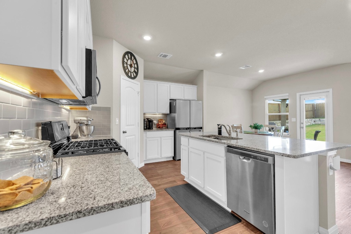 19525 Abigail Fillmore Road Manor, TX 78653 - Photo 8 of 40 Kitchen featuring decorative backsplash, light stone counters, stainless steel appliances, an island with sink, and white cabinetry