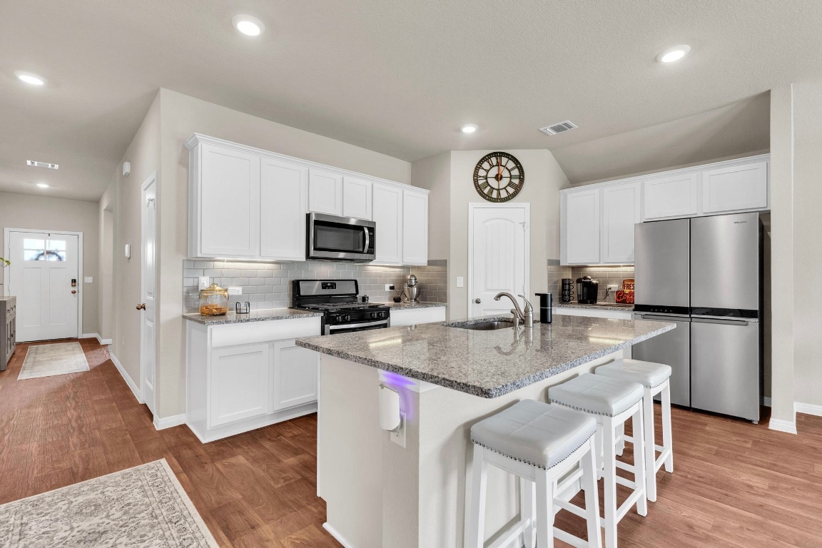 19525 Abigail Fillmore Road Manor, TX 78653 - Photo 9 of 40 Kitchen featuring white cabinetry, decorative backsplash, stainless steel appliances, a kitchen bar, and light stone counters