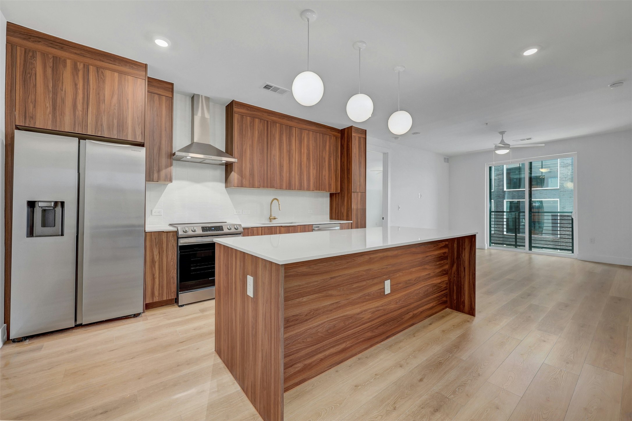 Kitchen with stainless steel appliances, wall chimney range hood, light countertops, a kitchen island, and light wood-style flooring