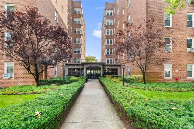a view of a brick building next to a big yard and large trees