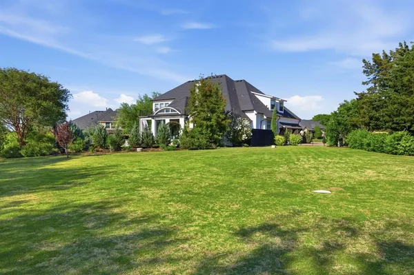 a view of a building in front of a big yard with plants and large trees