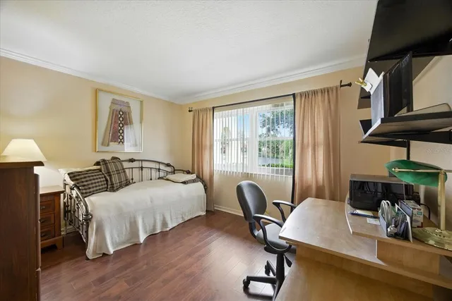 a bedroom with a bed a desk and chair with wooden floor