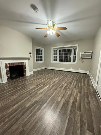 a view of an empty room with wooden floor fireplace and a window