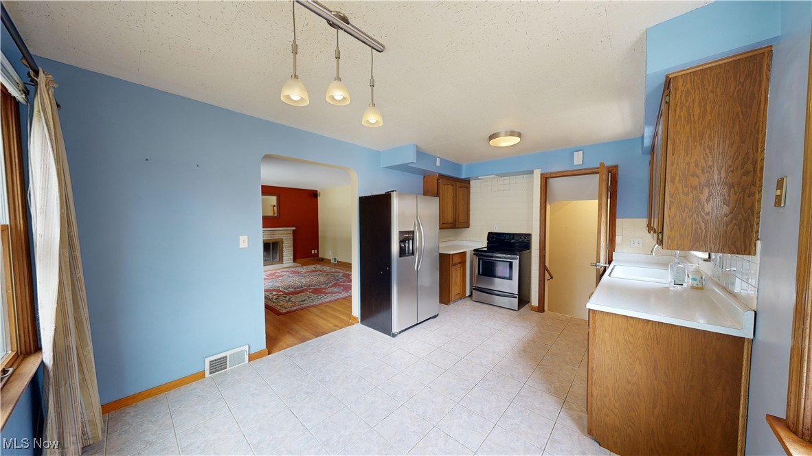 29280 White Road Wickliffe, OH 44092 - Photo 4 of 43 Eat in Kitchen featuring tasteful backsplash, hanging light fixtures, appliances with stainless steel finishes, light hardwood / wood-style flooring, and a brick fireplace
