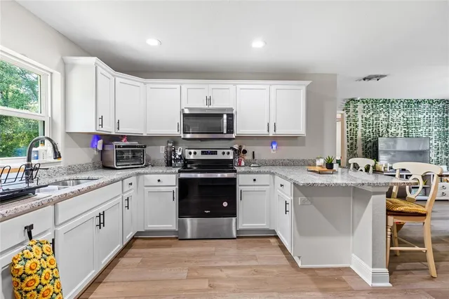 a kitchen with stainless steel appliances granite countertop a stove top oven a sink dishwasher and white cabinets with wooden floor