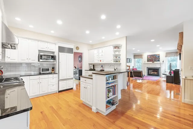 a kitchen with stainless steel appliances kitchen island granite countertop a stove top oven a sink a refrigerator and white cabinets with wooden floor