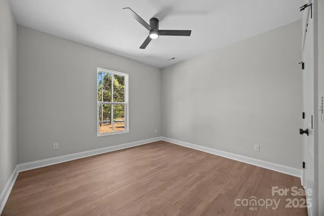 an empty room with wooden floor ceiling fan and windows