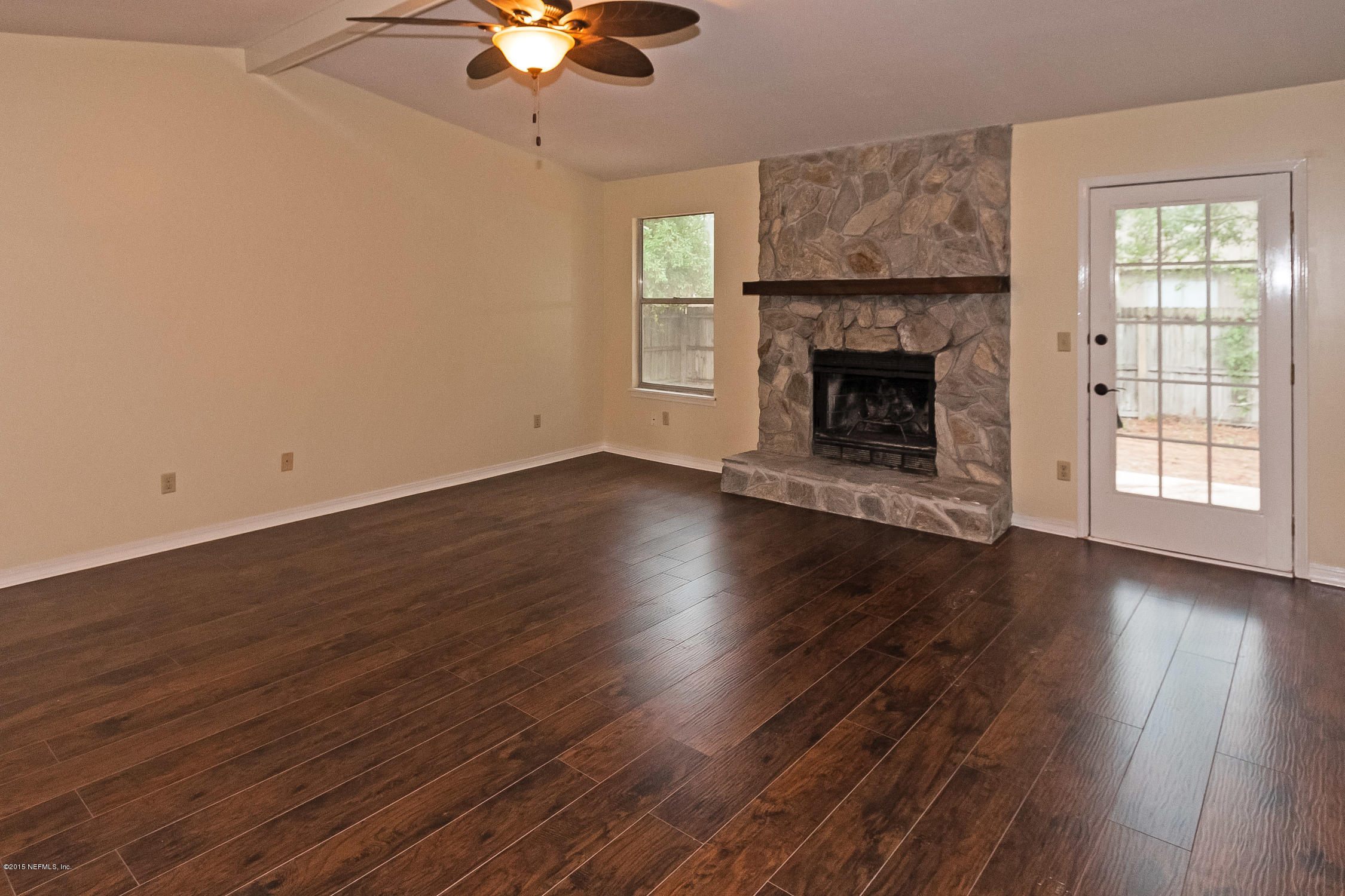1551 Derringer Road Jacksonville, FL 32225 - Photo 8 of 27 an empty room with wooden floor a fireplace a chandelier fan and windows