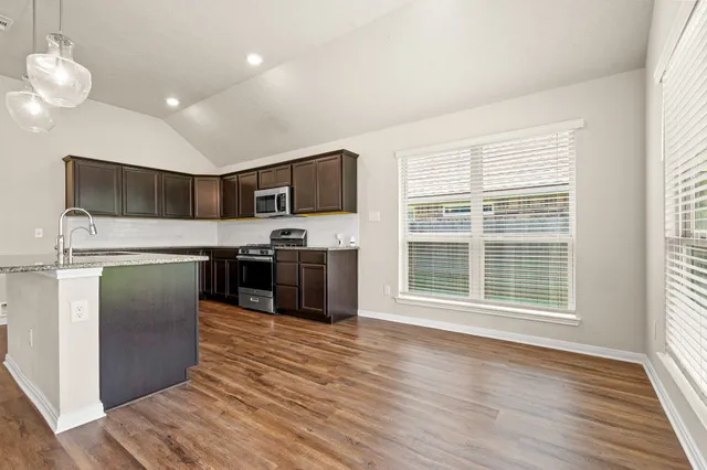 a kitchen with stainless steel appliances granite countertop a refrigerator a sink a stove top oven and a wooden floors