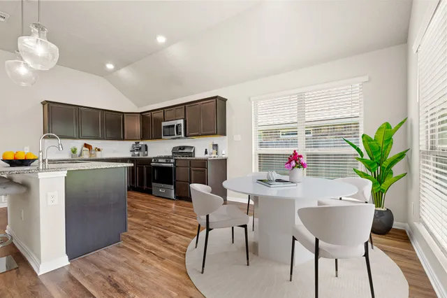 a room with stainless steel appliances kitchen island granite countertop a dining table chairs and a refrigerator