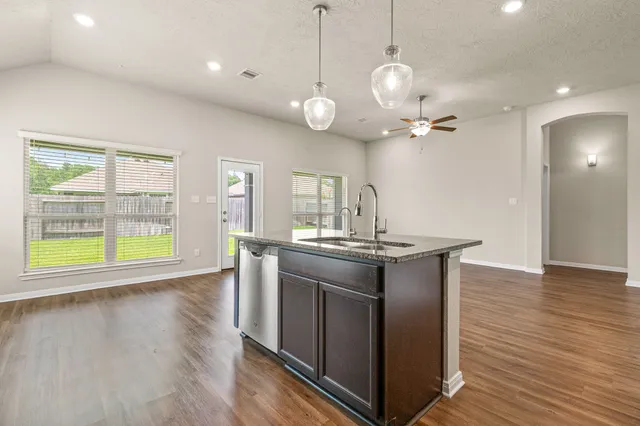 a view of an empty room and kitchen with wooden floor
