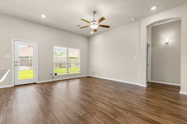 an empty room with wooden floor chandelier fan and windows