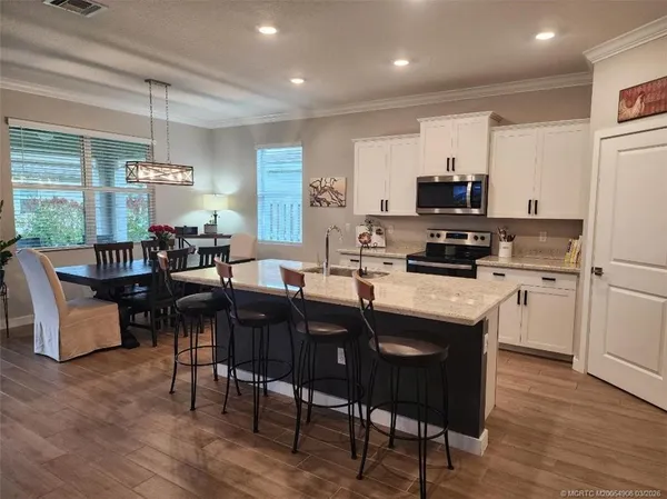 a kitchen with stainless steel appliances granite countertop a sink a stove a refrigerator a dining table and chairs with wooden floor