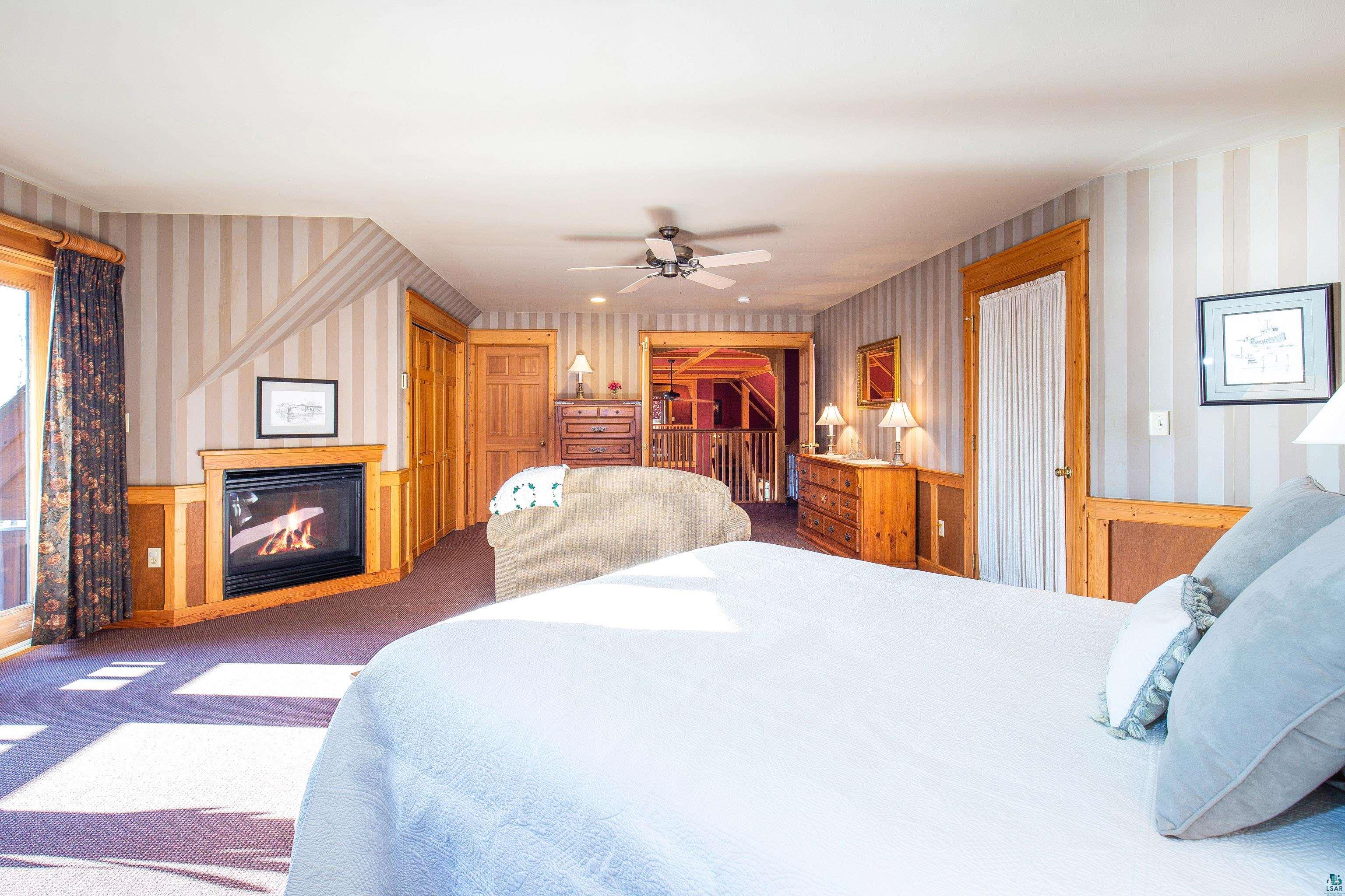 89405 Jack Pine Road Cornucopia, WI 54827 - Photo 54 of 60 Bedroom featuring wallpapered walls, carpet floors, a glass covered fireplace, and a ceiling fan