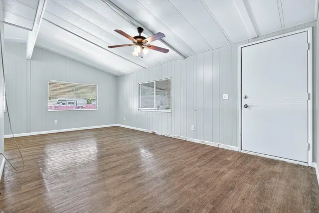 an empty room with wooden floor ceiling fan and windows