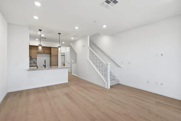 a view of an empty room with wooden floor and kitchen view