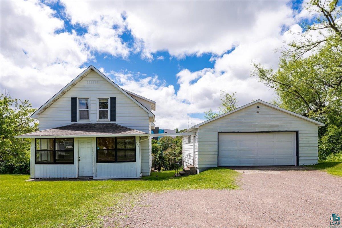 White two-story home featuring a covered front porch with dark-framed windows, a white entry door, and dark window shutters on the upper level 2 car garage.  To the left of the house is a double lot.