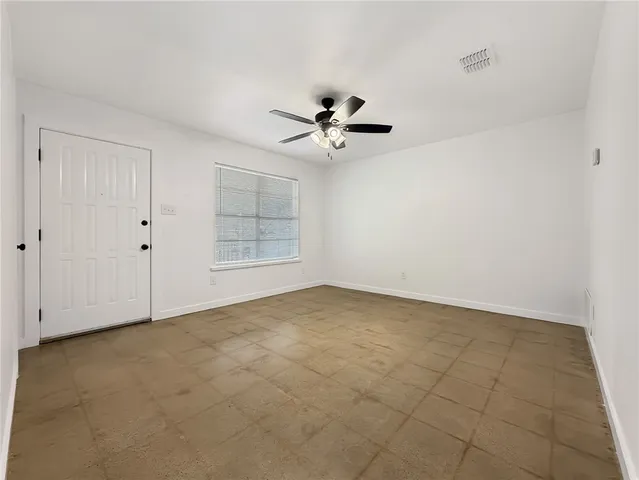 an empty room with chandelier fan and windows