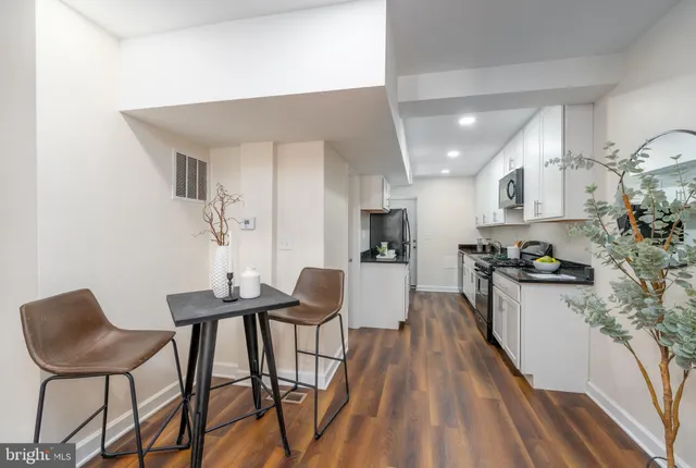 a kitchen with stainless steel appliances kitchen island granite countertop a dining table chairs and a refrigerator