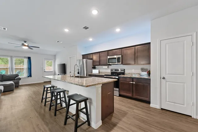 a kitchen with stainless steel appliances granite countertop a stove top oven a sink dishwasher a dining table and chairs with wooden floor