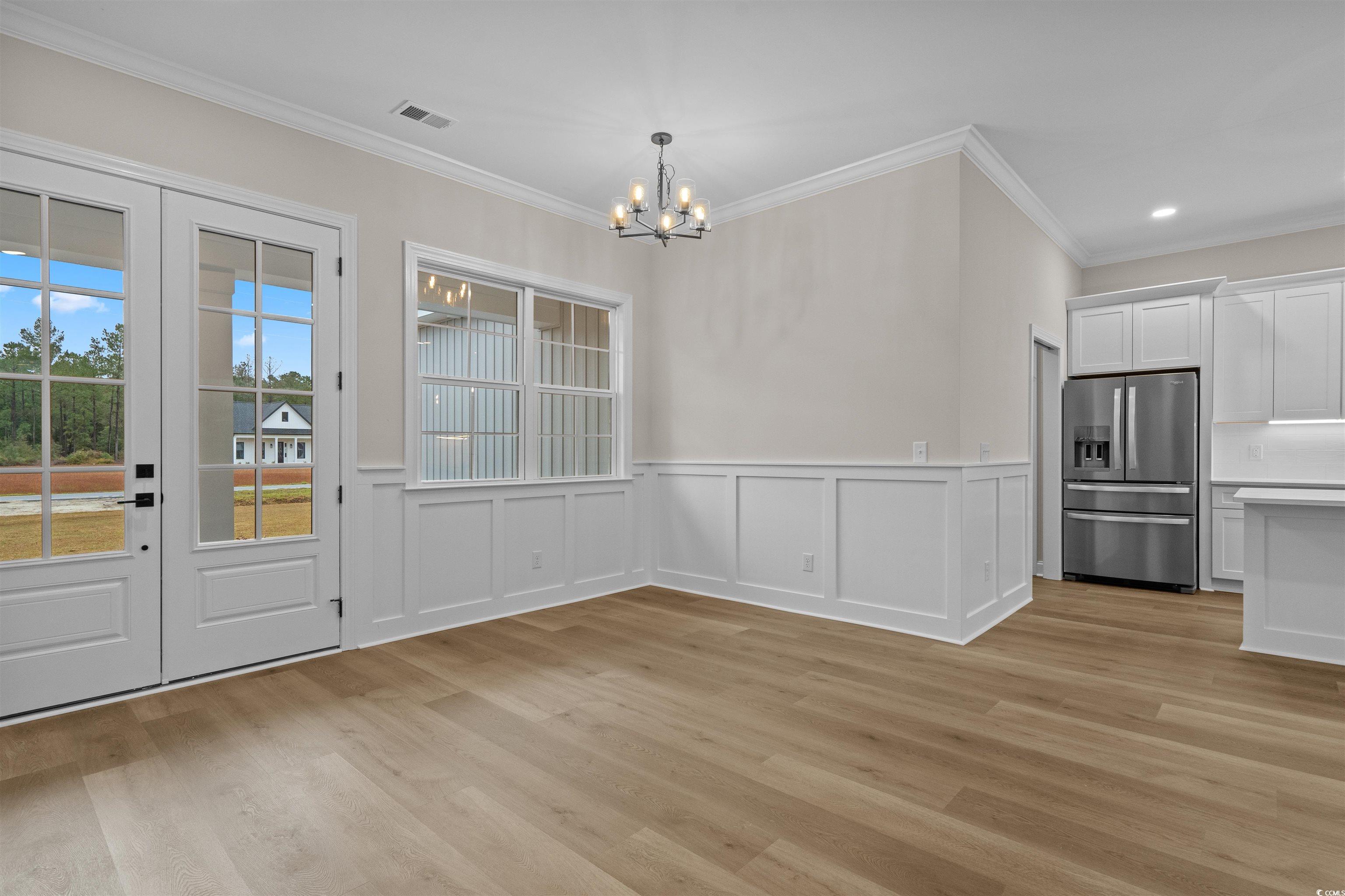 6927 Pauley Swamp Road Conway, SC 29527 - Photo 12 of 40 Unfurnished dining area featuring ornamental molding, a decorative wall, light wood finished floors, a wainscoted wall, and a chandelier