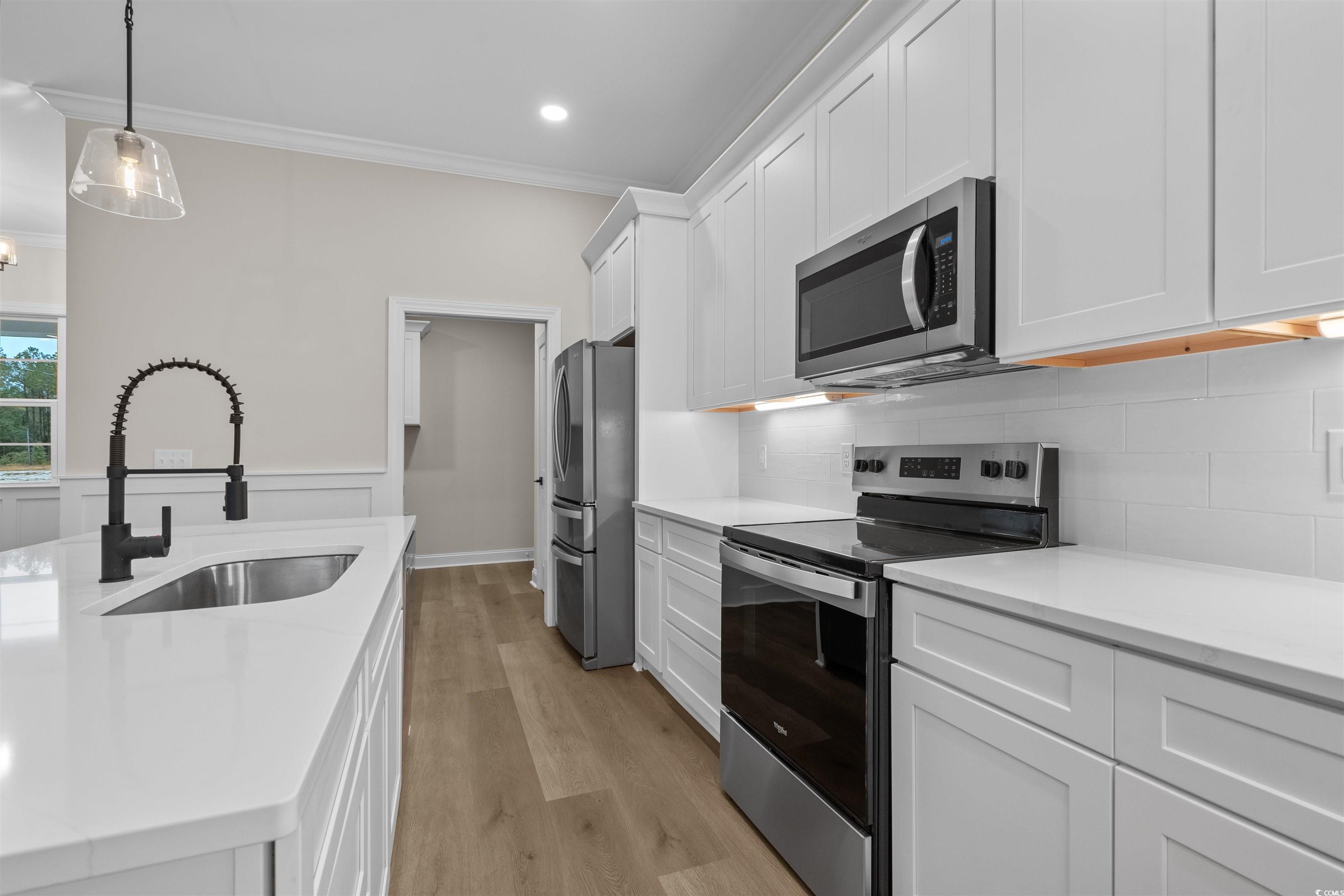 6927 Pauley Swamp Road Conway, SC 29527 - Photo 15 of 40 Kitchen featuring stainless steel appliances, light wood-style flooring, hanging light fixtures, tasteful backsplash, and crown molding