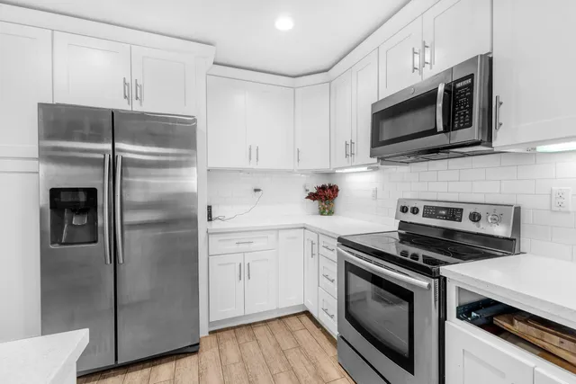 a kitchen with stainless steel appliances kitchen island granite countertop a refrigerator a stove a dining table and chairs with wooden floor