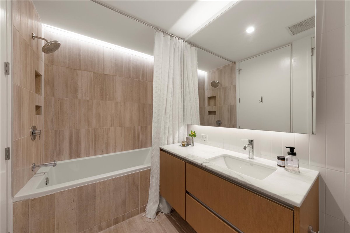 313 West 17th Street, Unit 1104 Austin, TX 78701 - Photo 17 of 40 Contemporary second bath featuring a sleek double vanity with custom marble counters, modern fixtures and a soaking tub/shower combination wrapped in warm, textured tile. A refined and functional space designed for guests or everyday living.