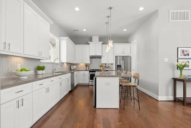 a kitchen with stainless steel appliances kitchen island granite countertop a stove a sink a refrigerator and white cabinets with wooden floor